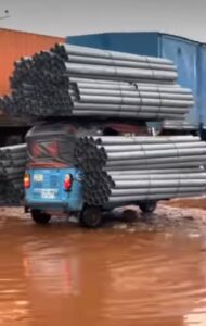 Keke rider struggles on damaged road after overloading his tricycle with aluminum rods (VIDEO)