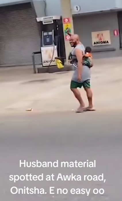 "Husband material" – Man spotted joyfully strolling with a child on his back in Onitsha (WATCH)